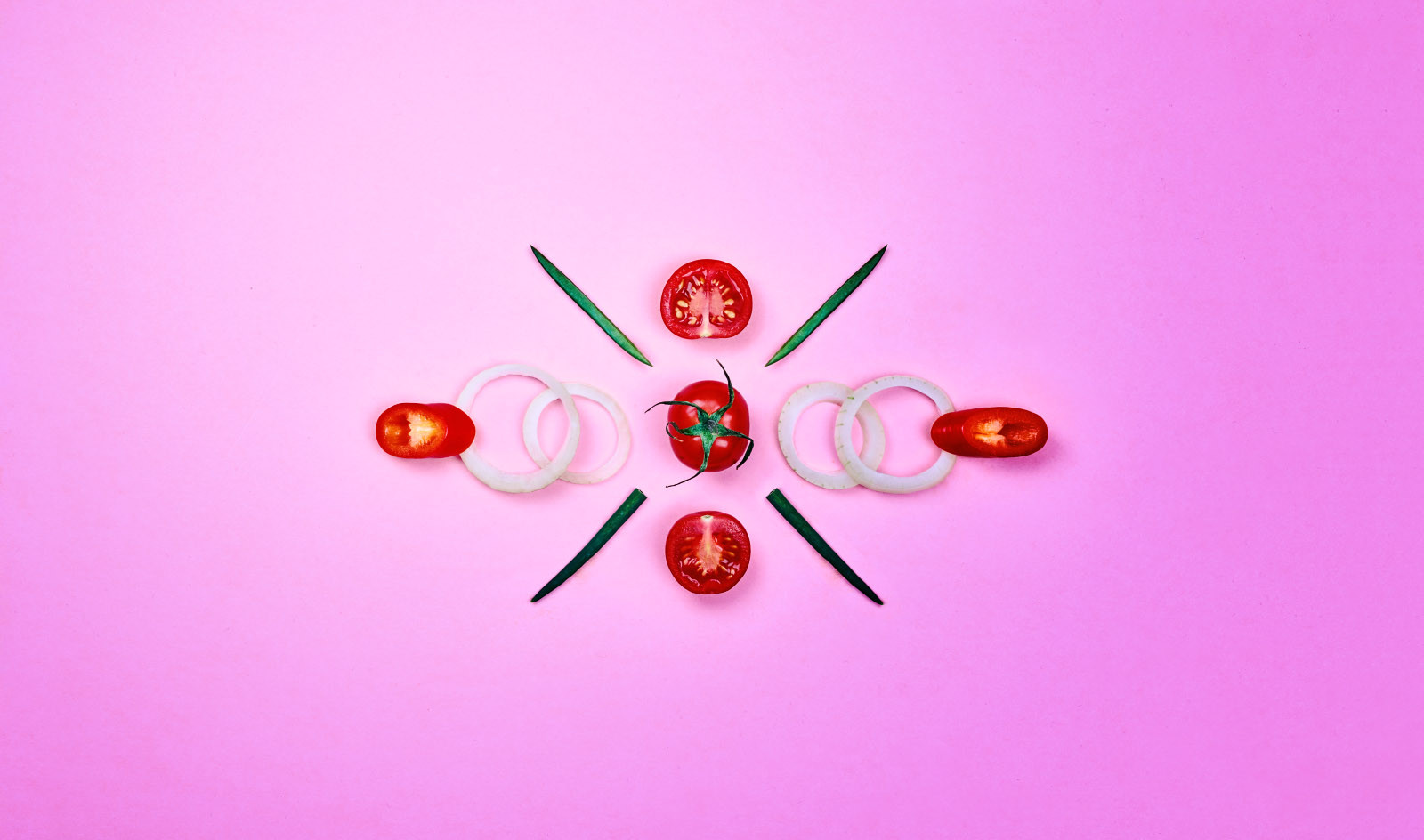 Tomaten und Zwiebeln arrangiert auf rosa Untergrund.