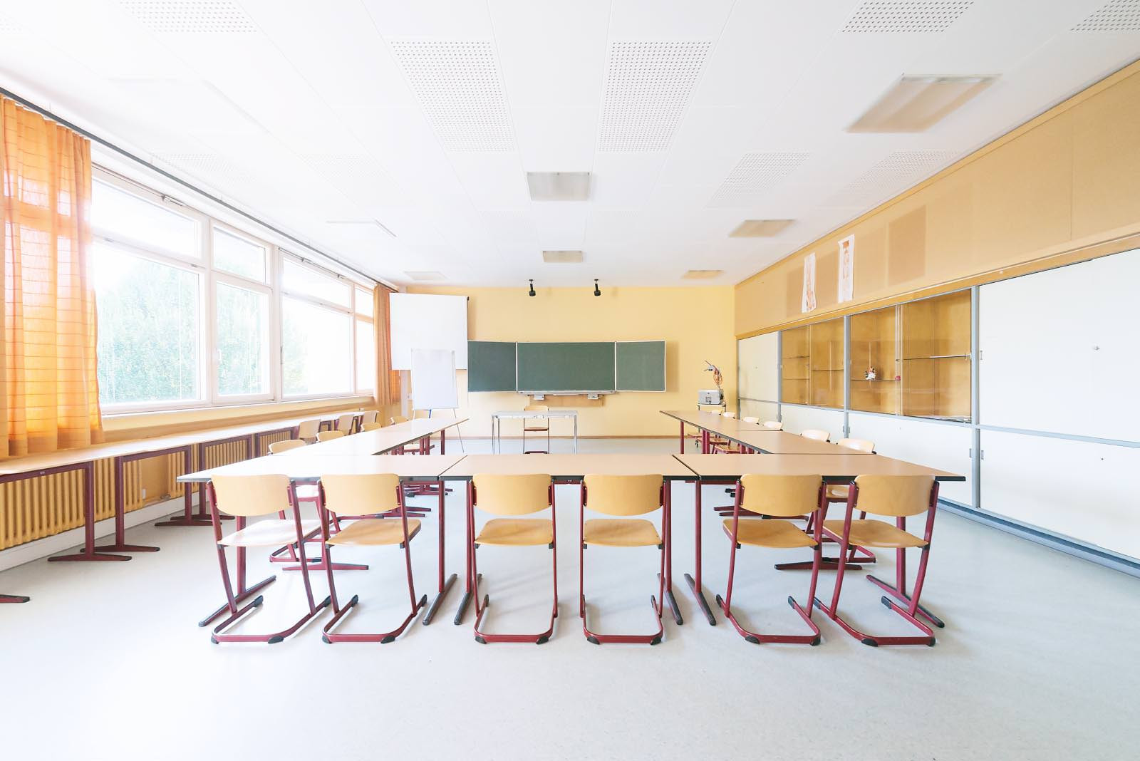 Klassenzimmer mit gelber Wand, Tafel und Schaukasten