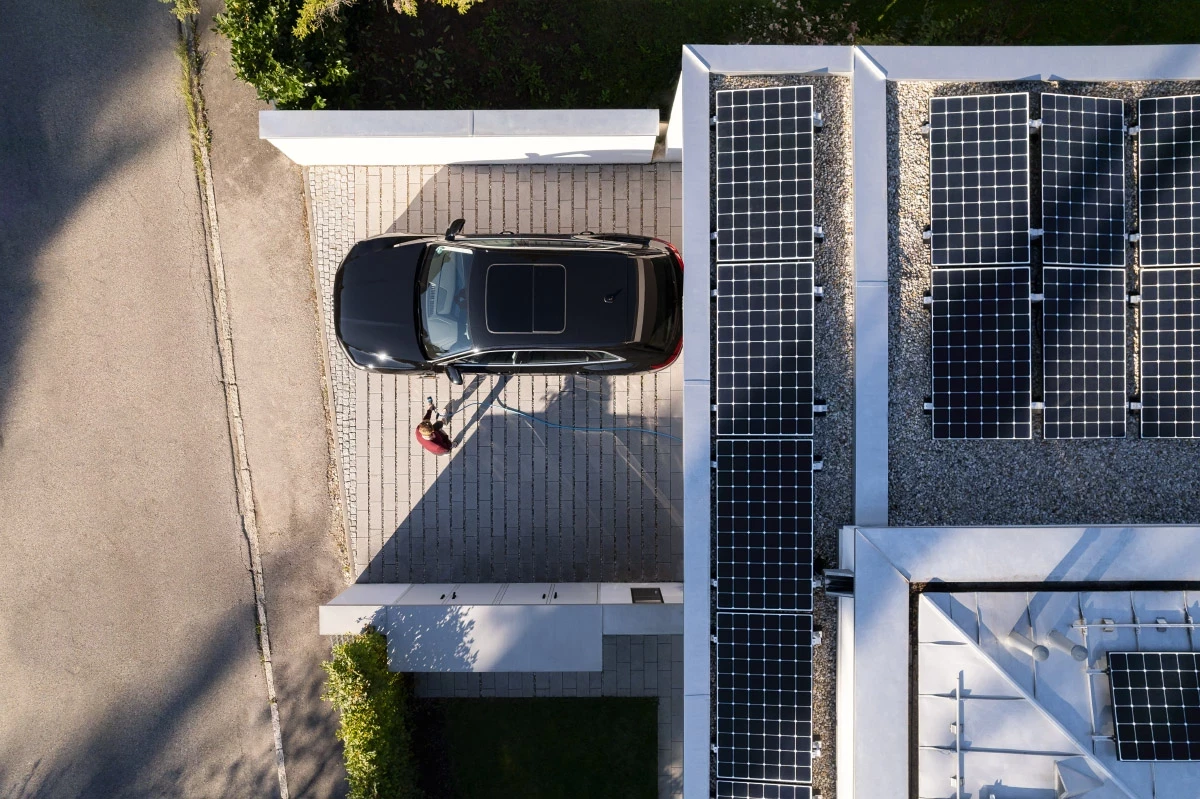 Top down Fotografie eines Hauses mit Solarpanels auf dem Dach. E-Auto vor der Garage