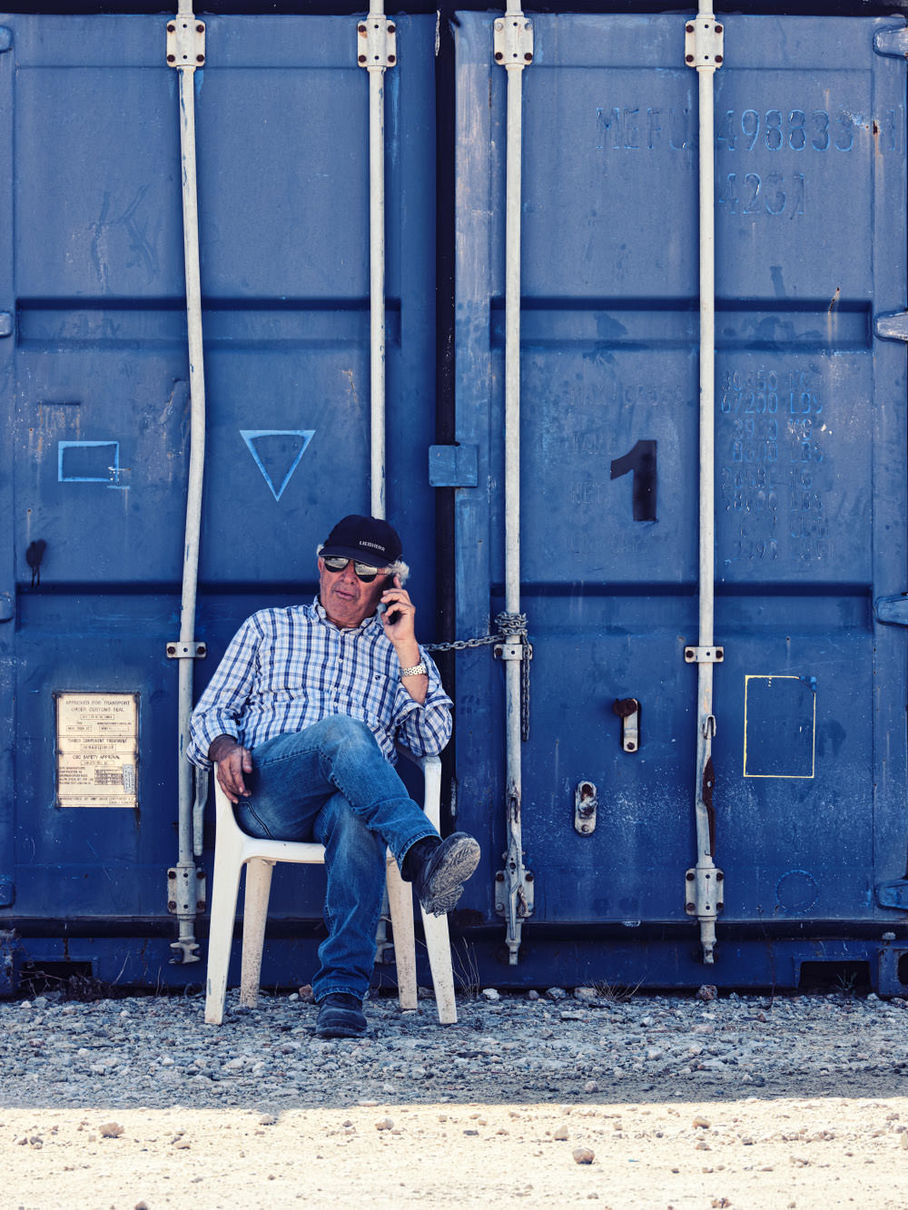 Herr Marnelakis (Senior) sitzt vor einem Frachtcontainer und telefoniert